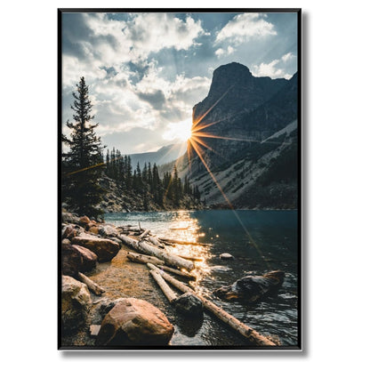 Das gerahmte Bild in den Maßen 50x70xm zeigt eine wunderschöne Landschaft in lebendigen Farben und ist in Sonnenlicht getaucht. Das Bild zeigt einen Fluss und Berge mit Tannen. Am Flussufer befinden sich kleiner Felsbrocken und Holzstämme. Der Blick ist in die Ferne gerichtet und Sonnenstrahlen liegen über der Landschaft.